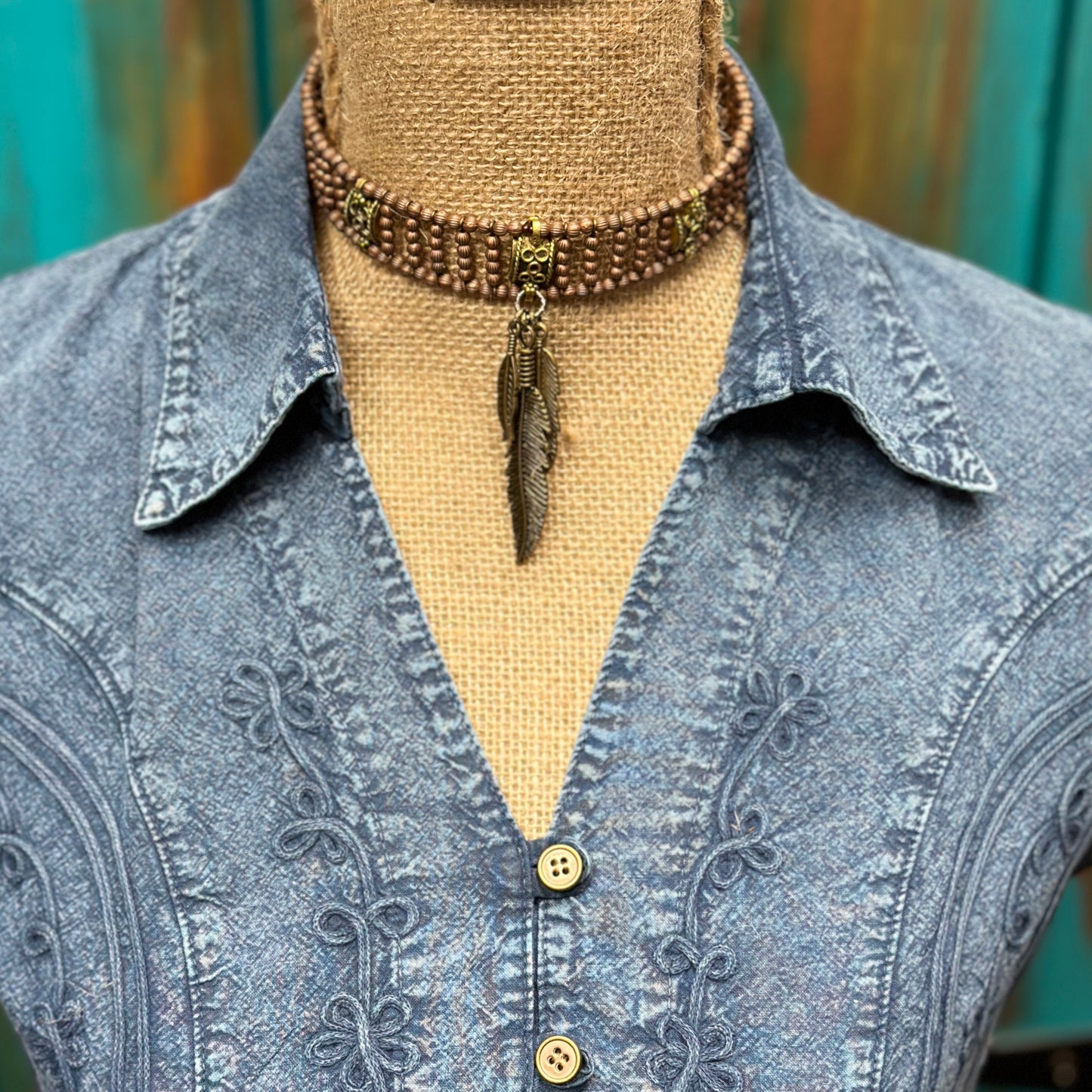 Brown beaded choker necklace with feather pendant on denim shirt.