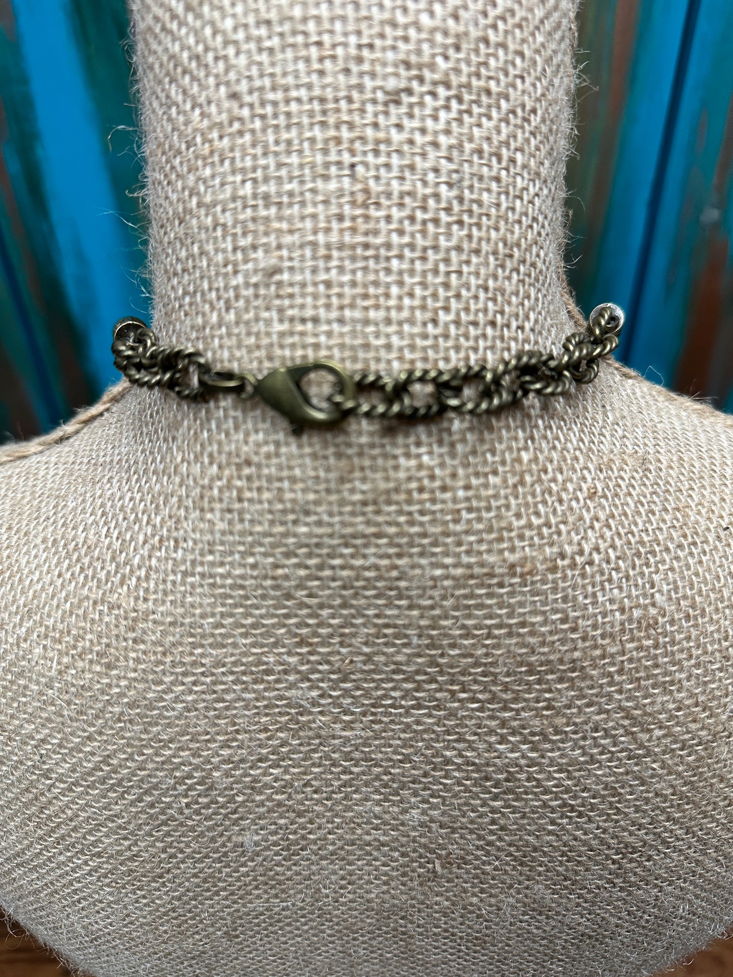 Close-up of a bronze-colored chain necklace clasp on a burlap-covered neck form.