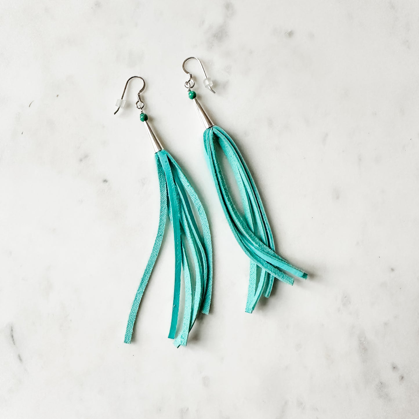 Turquoise leather tassel earrings on a white surface.
