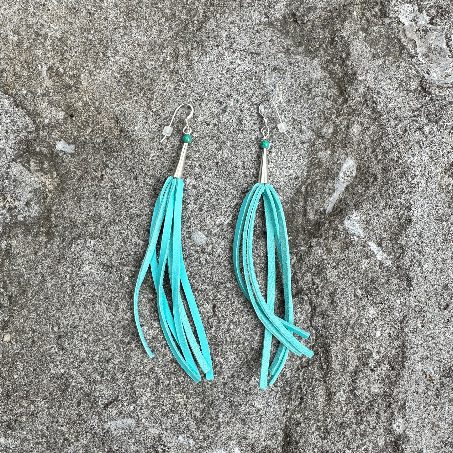 Turquoise tassel earrings on stone surface.