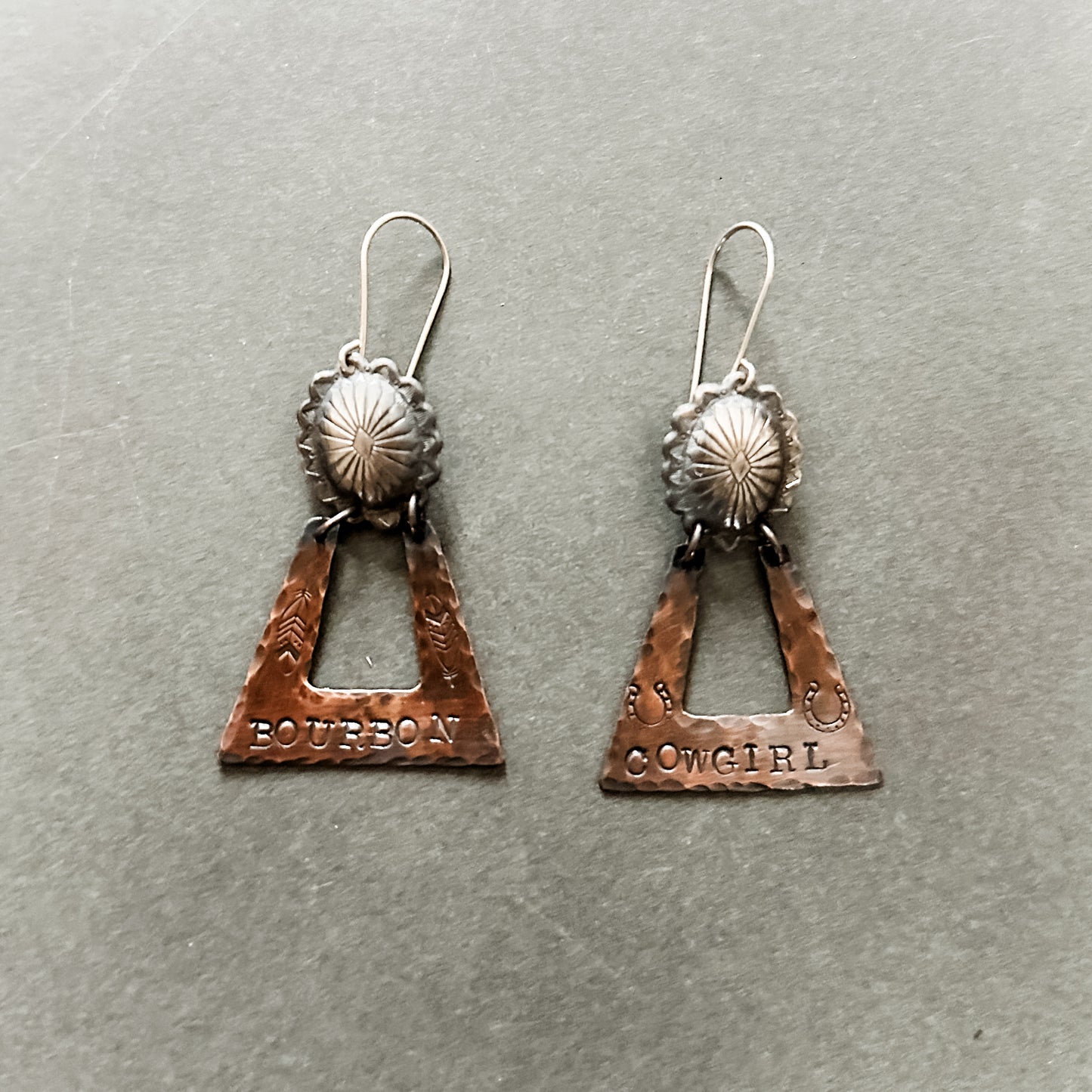 Two copper earrings with Bourbon and Cowgirl text.