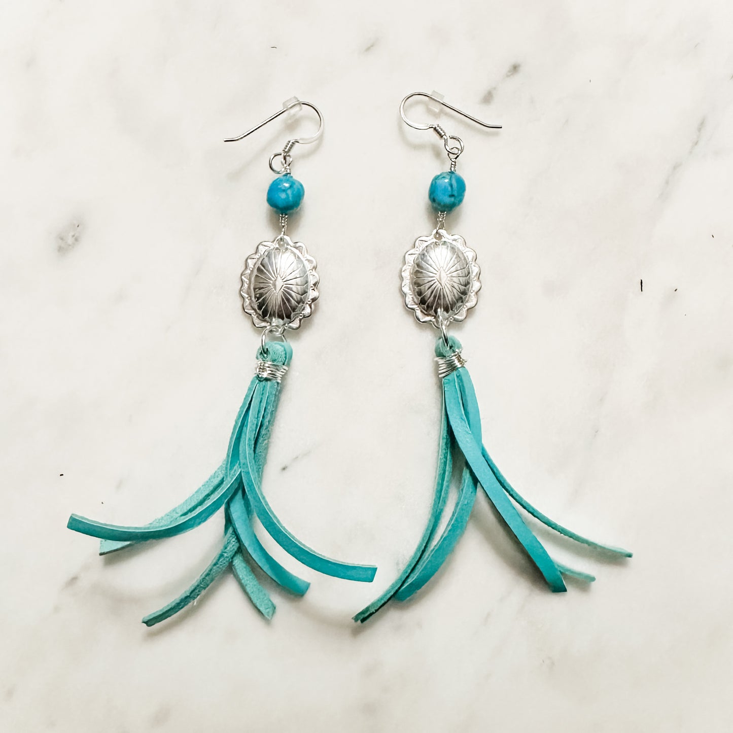Turquoise leather tassel earrings with silver accents.