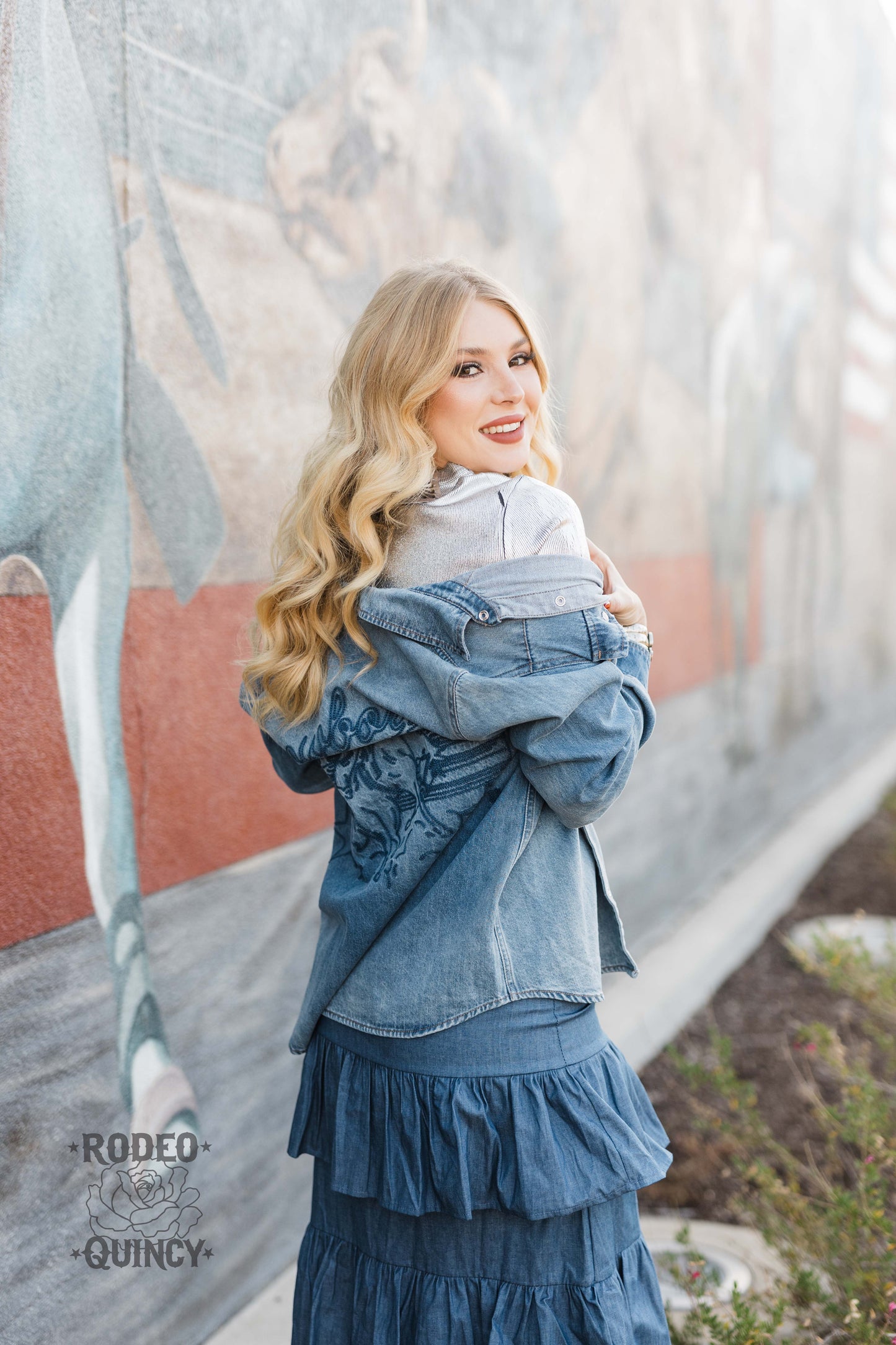 Smiling blonde in denim outfit, mural background