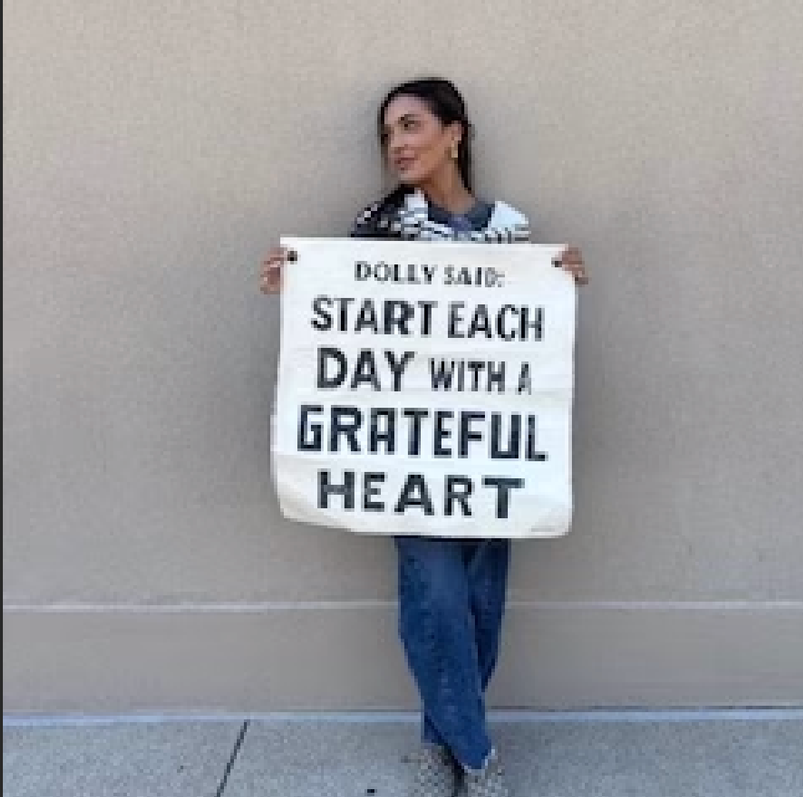 Woman holding Start each day with a grateful heart sign, April 18 screenshot.