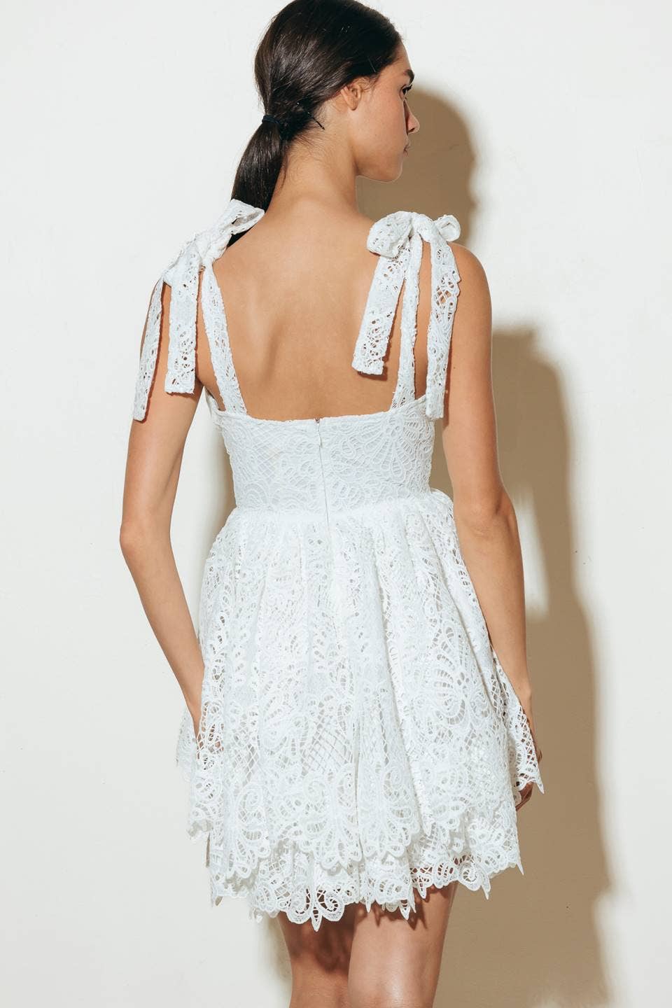 Woman wearing a white lace dress with bow straps.