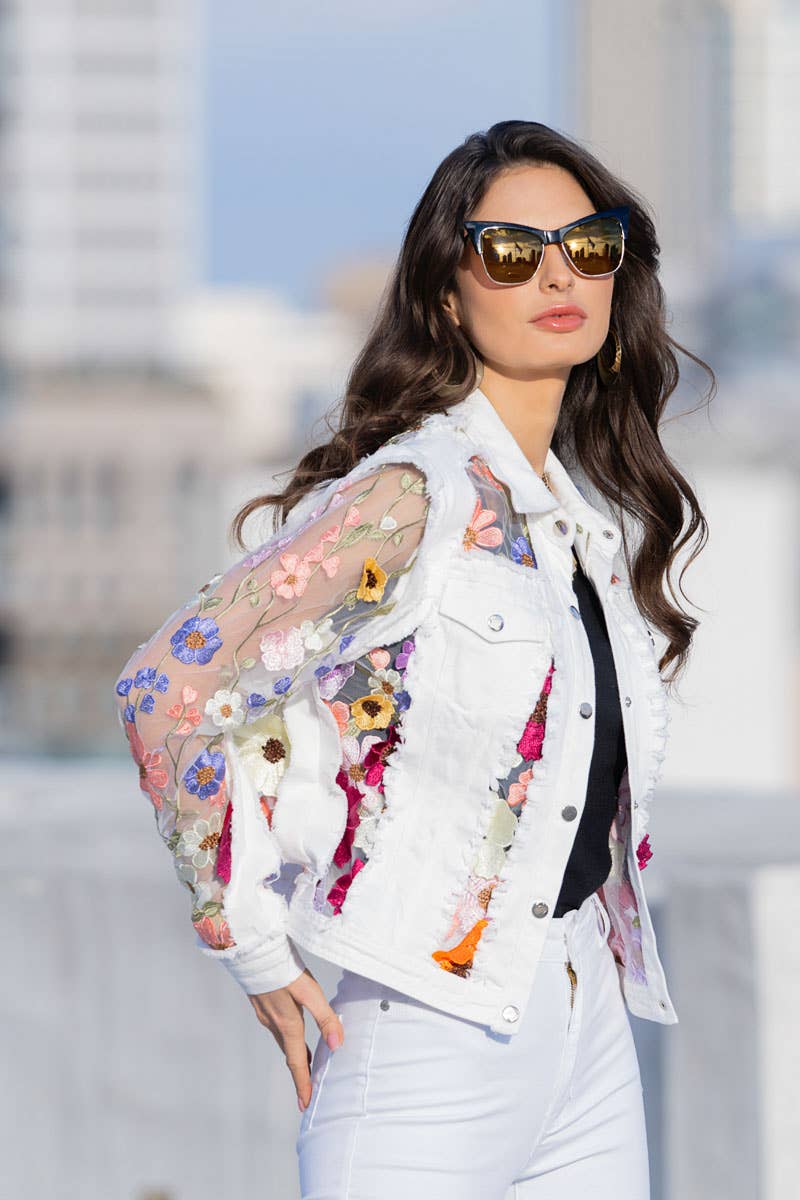 Woman in white floral denim jacket and sunglasses.