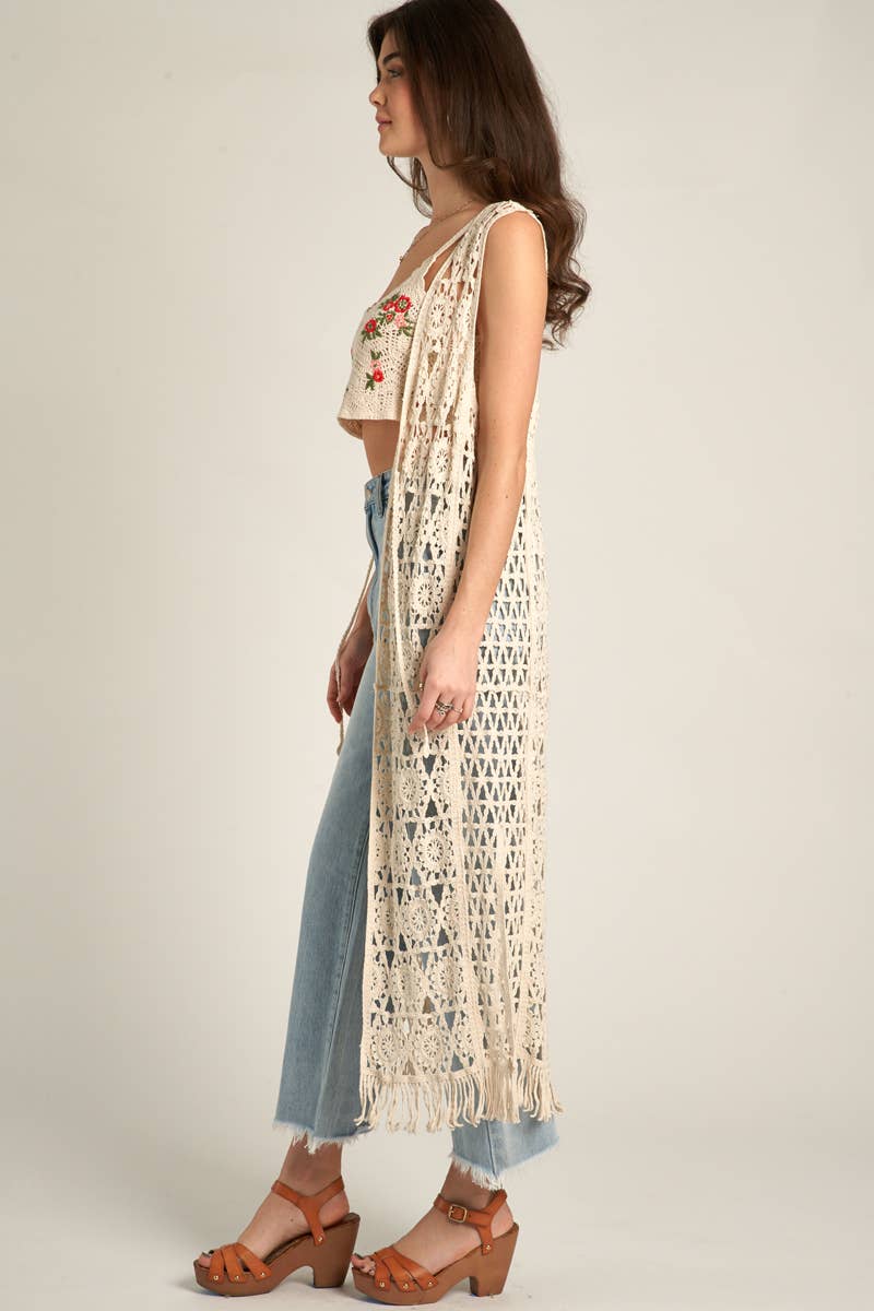 Woman in jeans, crop top, and crochet vest.