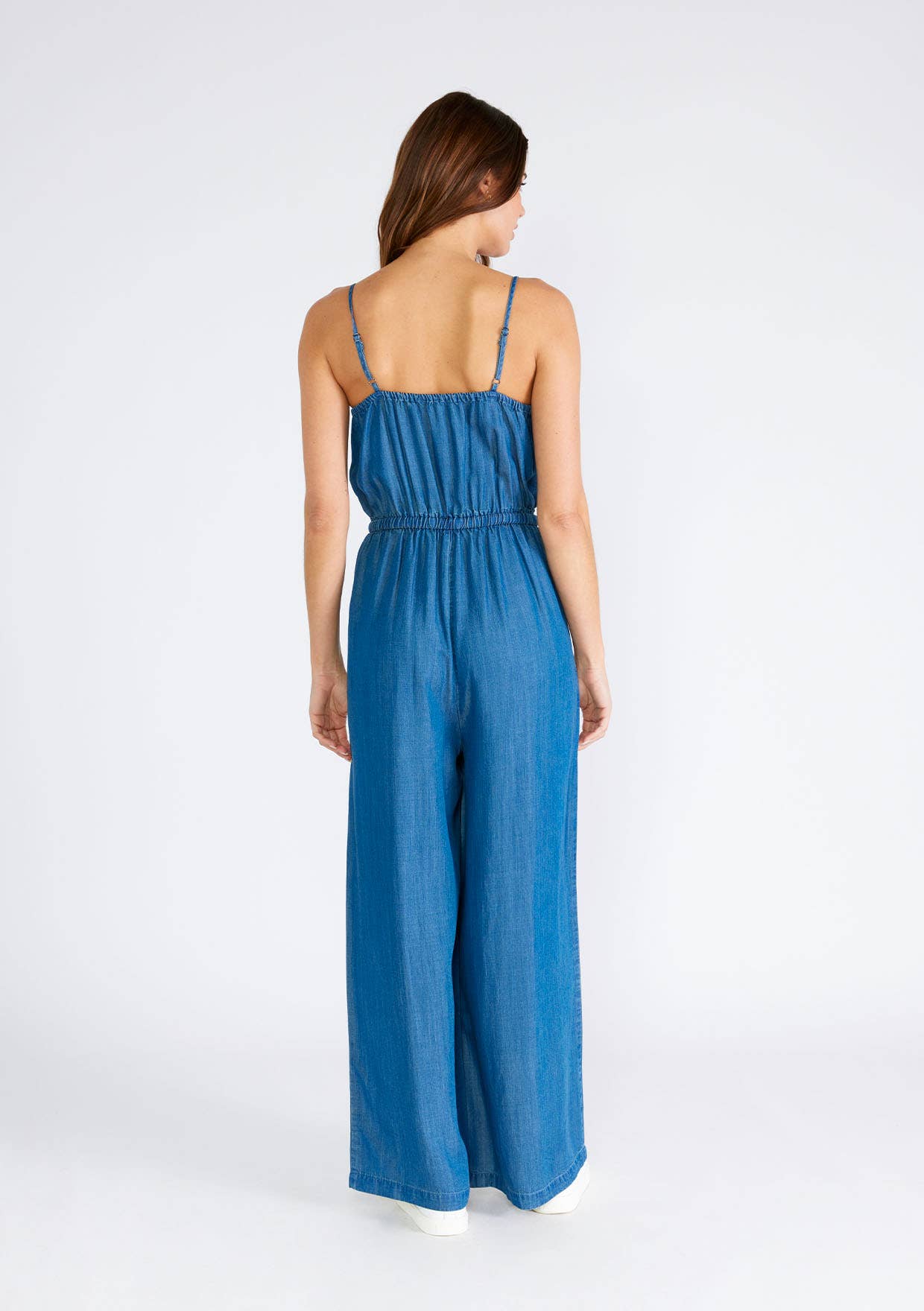 Woman wearing a blue denim jumpsuit, standing with back to camera.