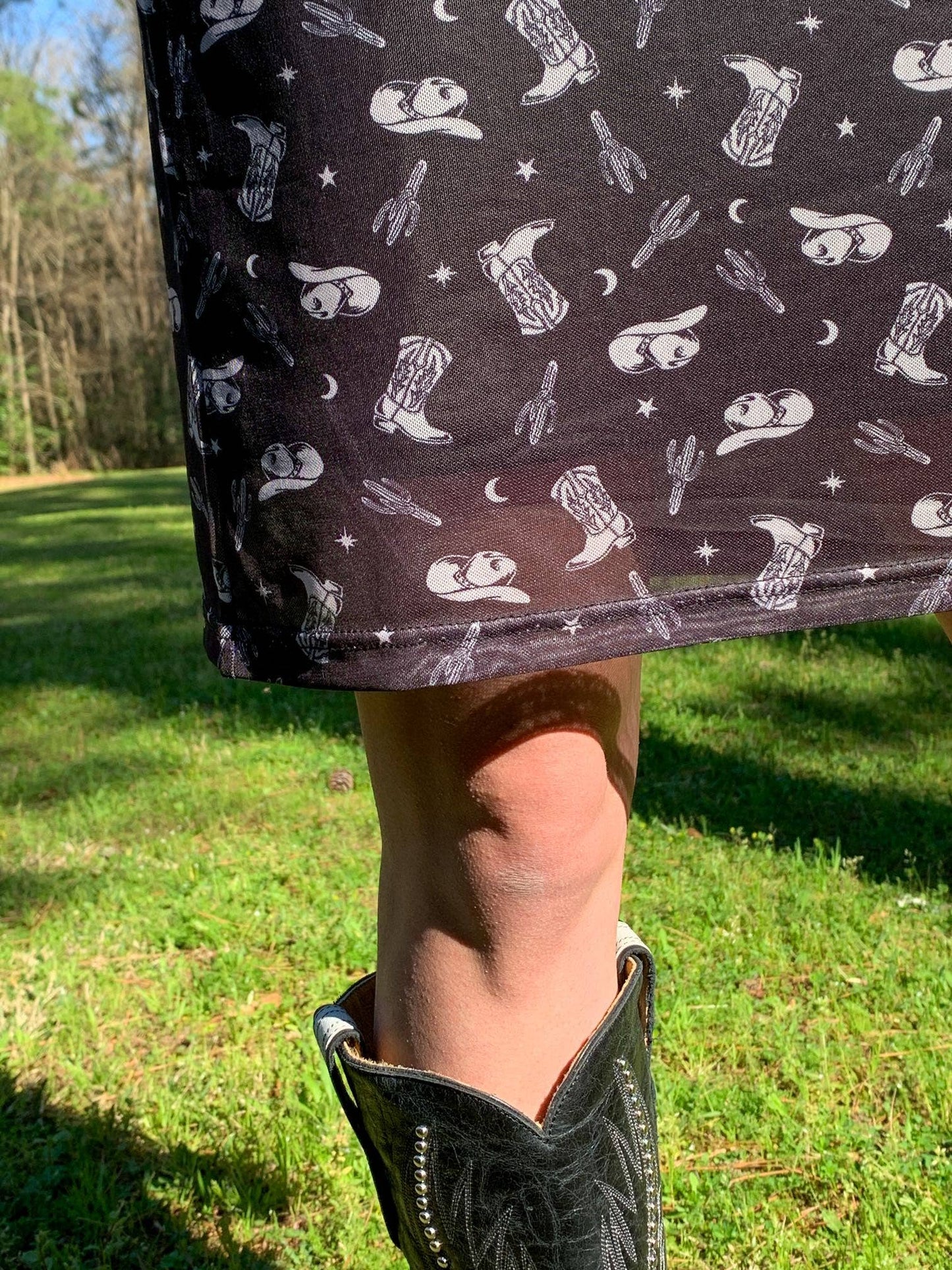 Woman's leg wearing a black cowboy boot and skirt with cowboy-themed pattern.