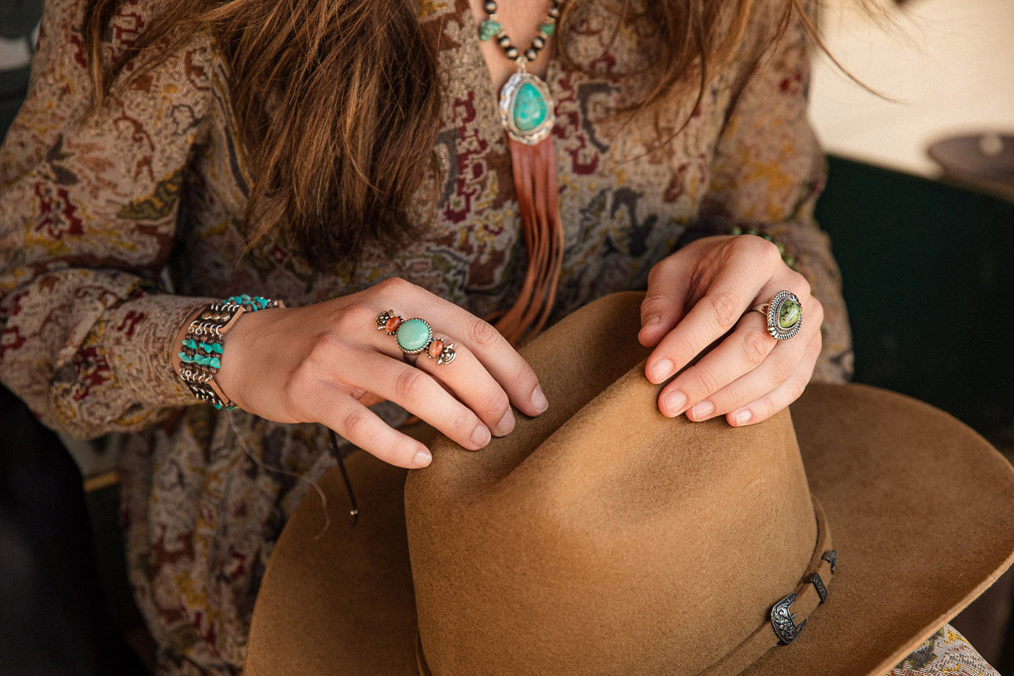 Woman holding cowboy hat, wearing turquoise jewelry, lifestyle image.