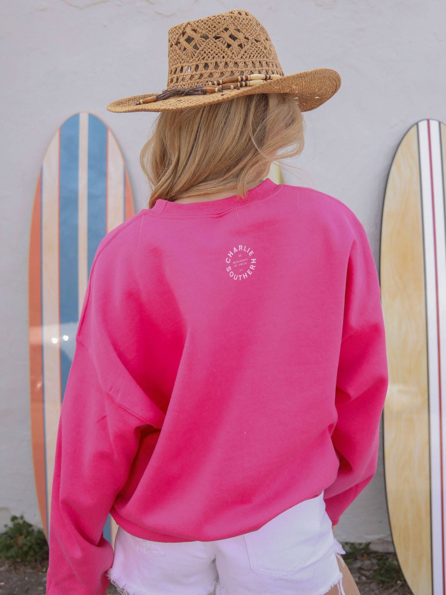Woman wearing a pink sweatshirt and straw hat, with surfboards.