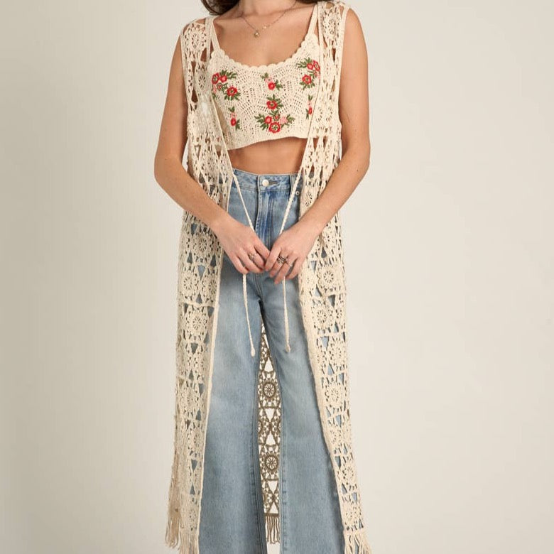 Woman in crocheted vest and top, jeans.