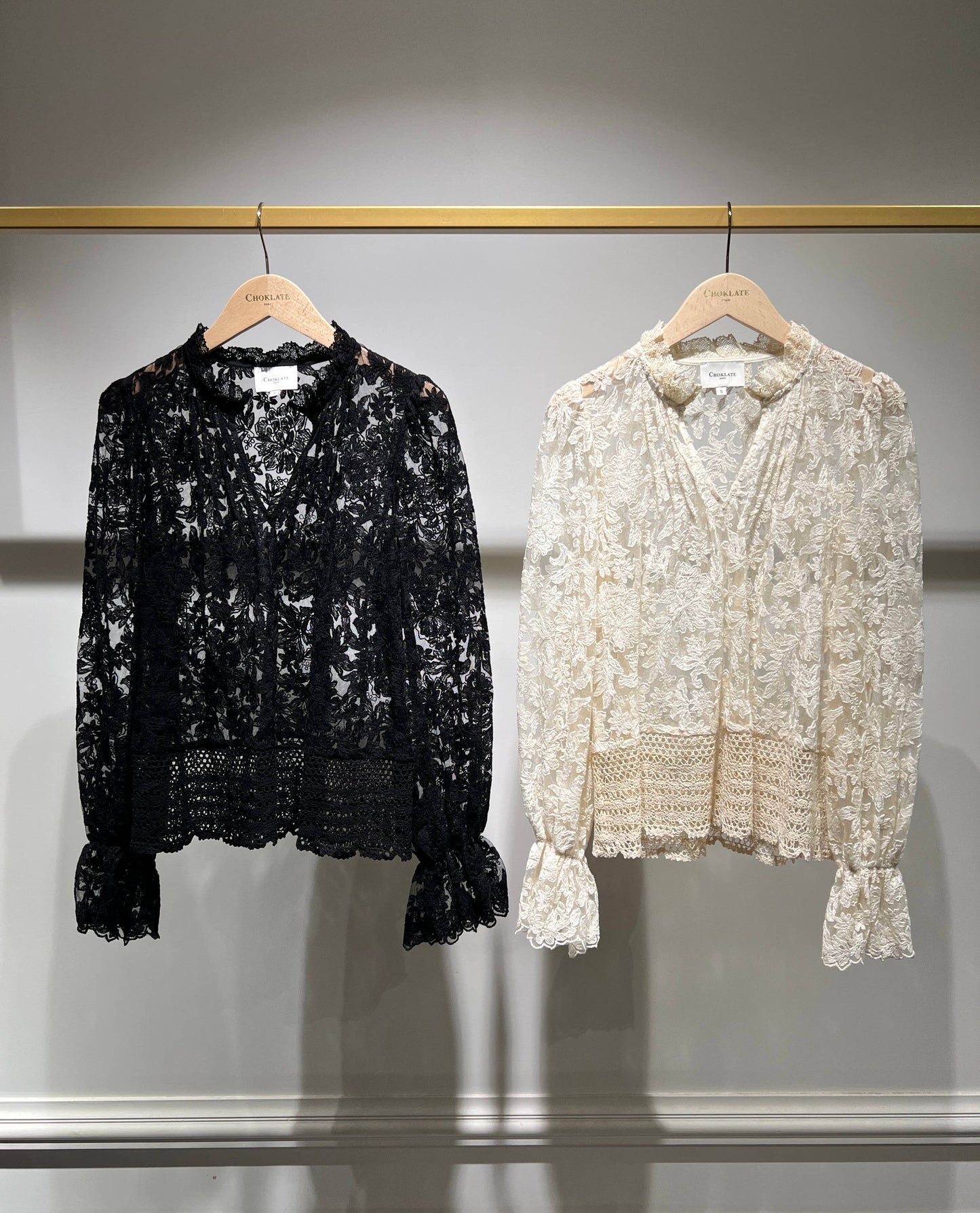 Two lace blouses hanging on a rack.