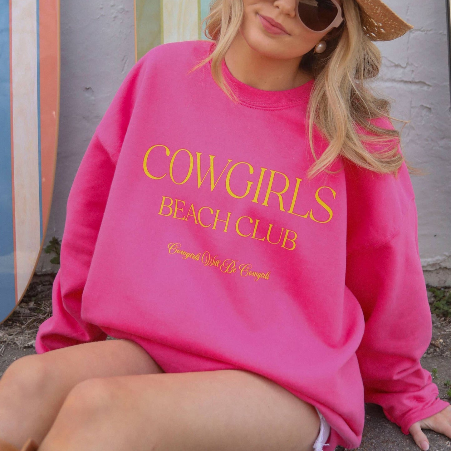 Woman in pink sweatshirt with Cowgirls Beach Club text.
