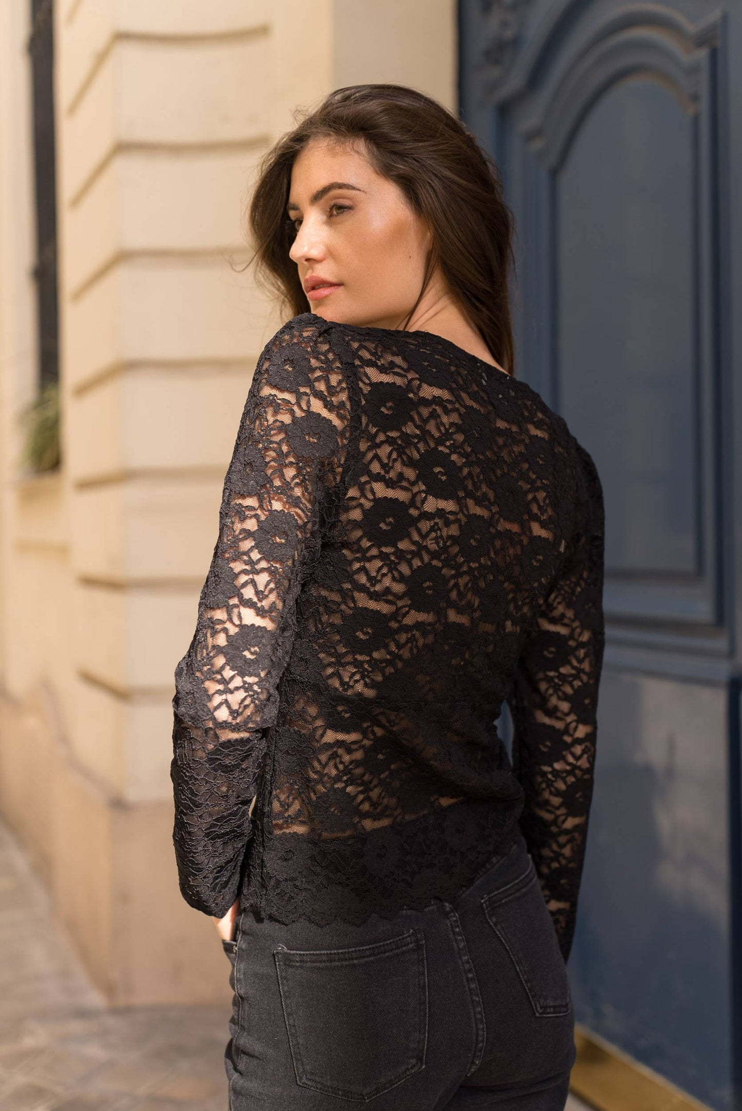 Woman in black lace top and jeans, looking over her shoulder.