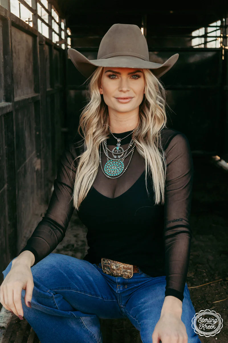 Woman in cowboy hat, mesh top, and jeans.