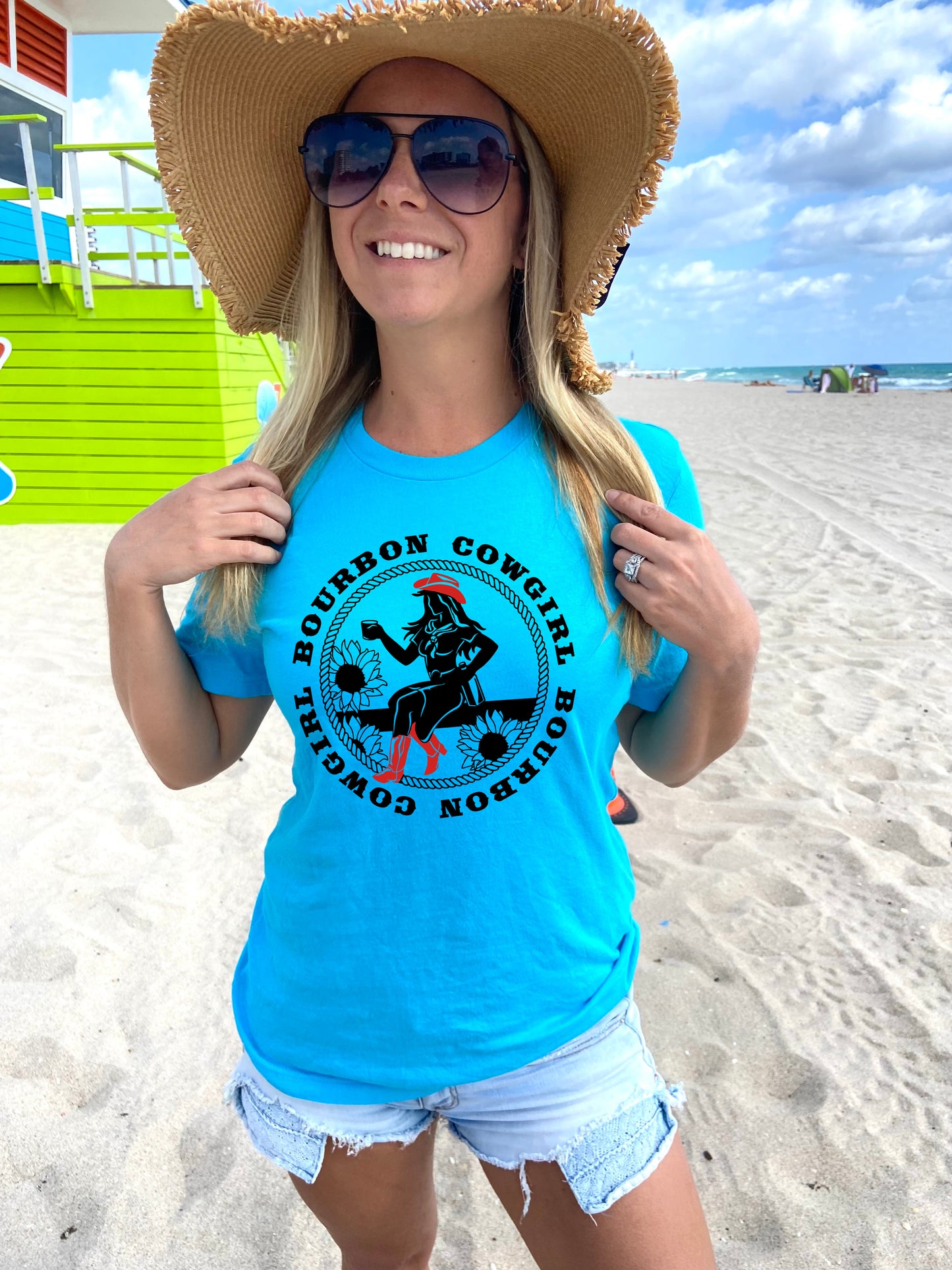 Woman wearing turquoise Bourbon Cowgirl tee, sunglasses, and straw hat