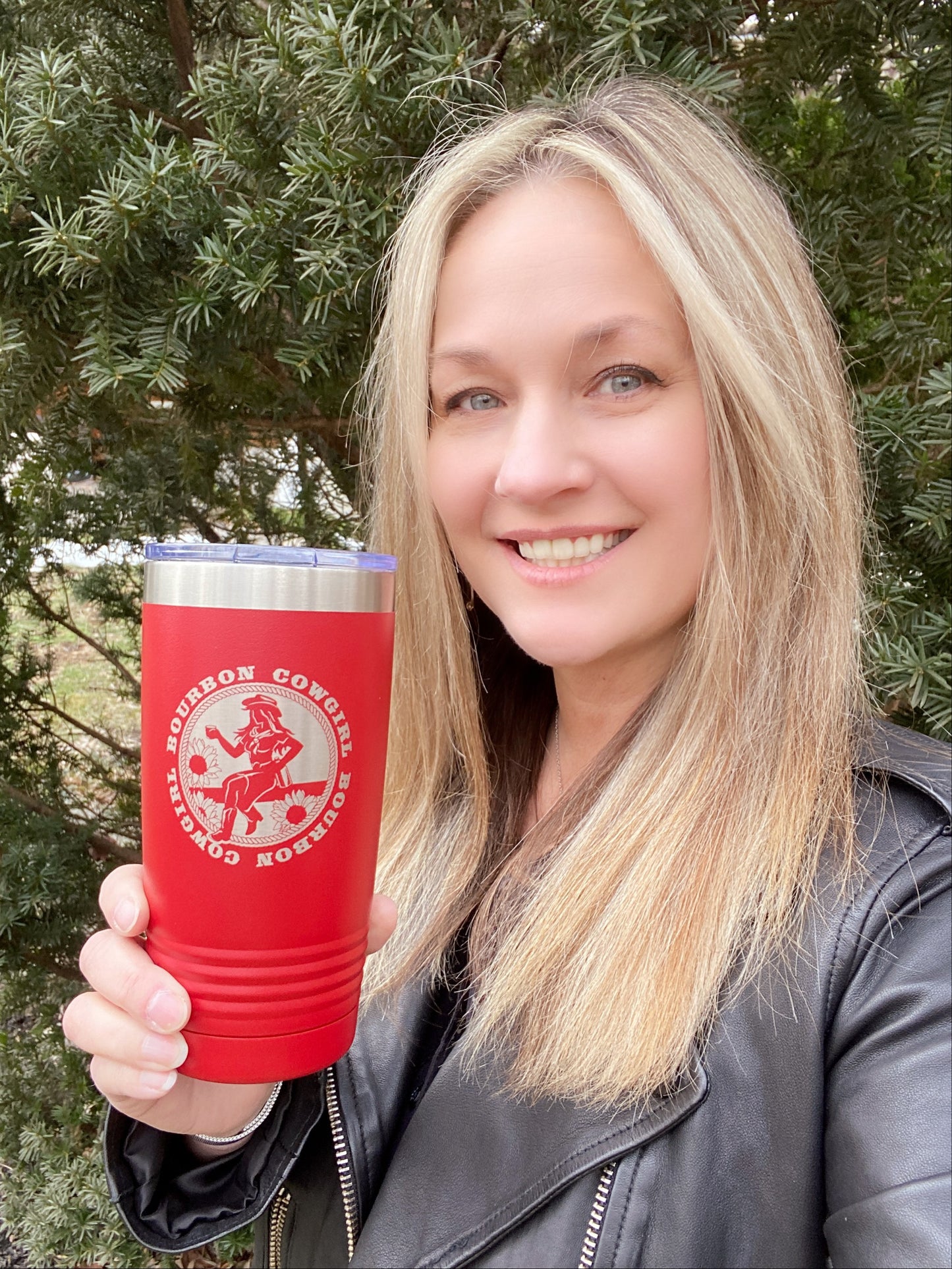Woman smiling, holding a red tumbler with a logo.