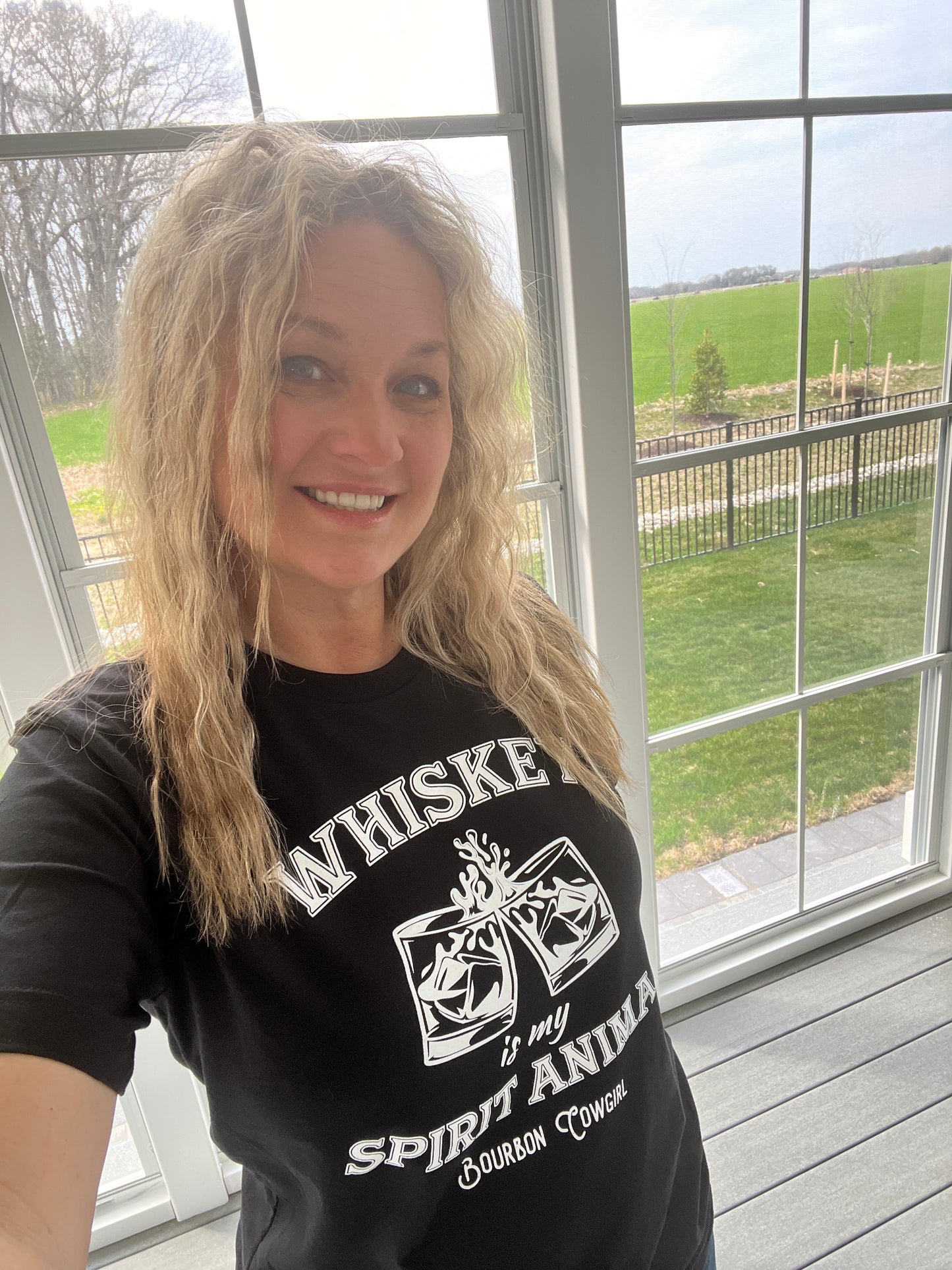 Woman in black t-shirt smiling near a window.