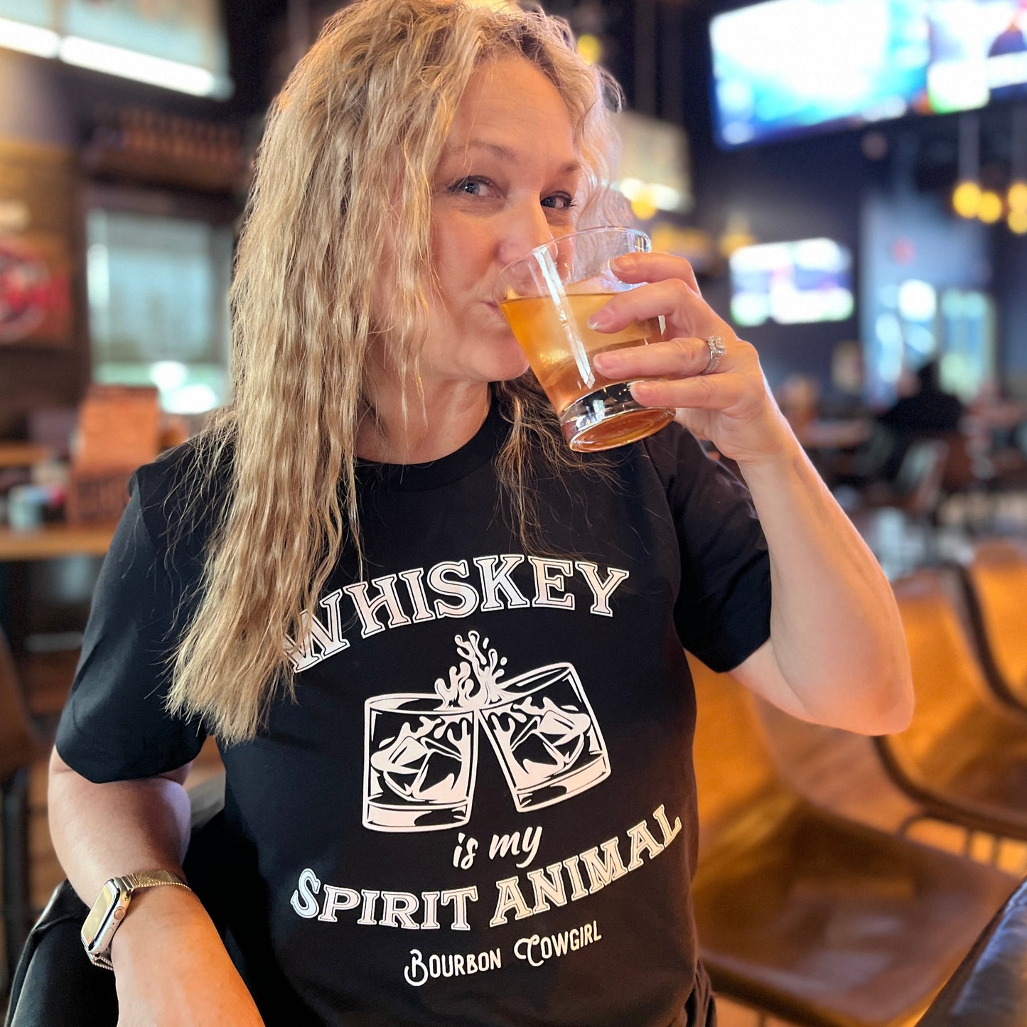 Woman drinking a beverage, wearing a Whiskey t-shirt.