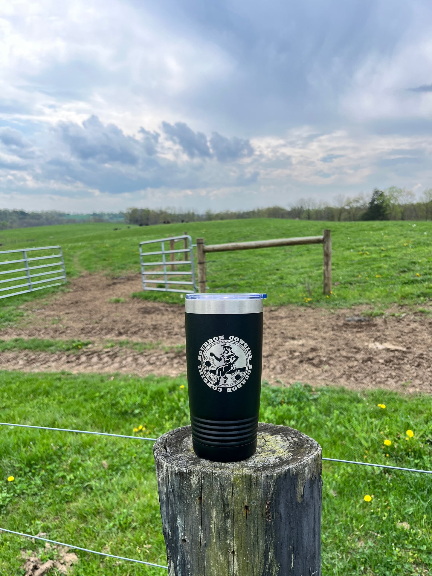 Black tumbler on a wooden post in a field.