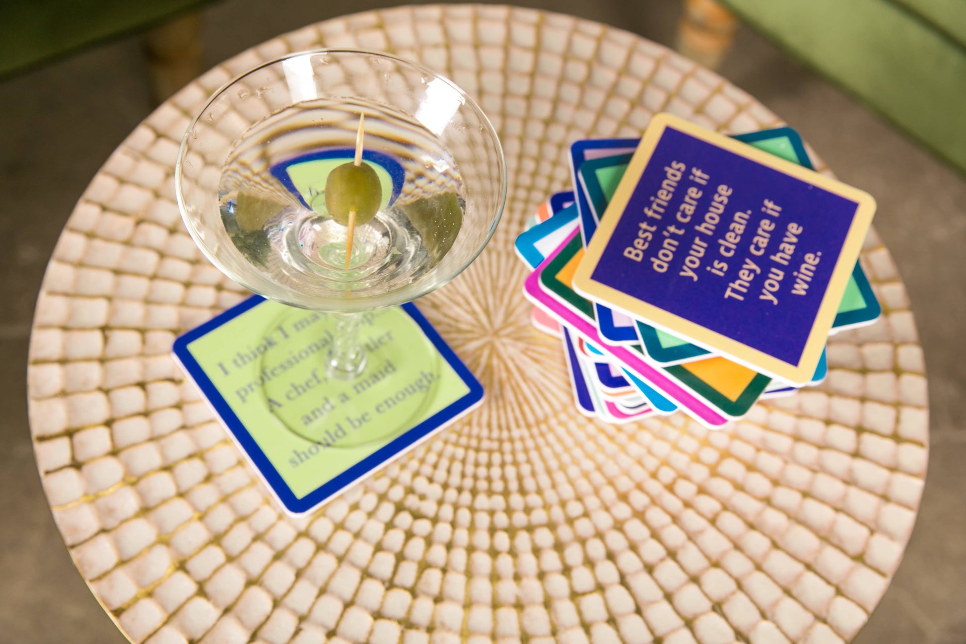 Martini with olive on a coaster next to a stack of quote coasters.