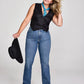 Woman in jeans, vest, and bandana holding a hat.