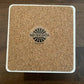 Square cork coaster with white trim and logo.