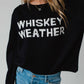 Woman wearing a black sweater that says Whiskey Weather.