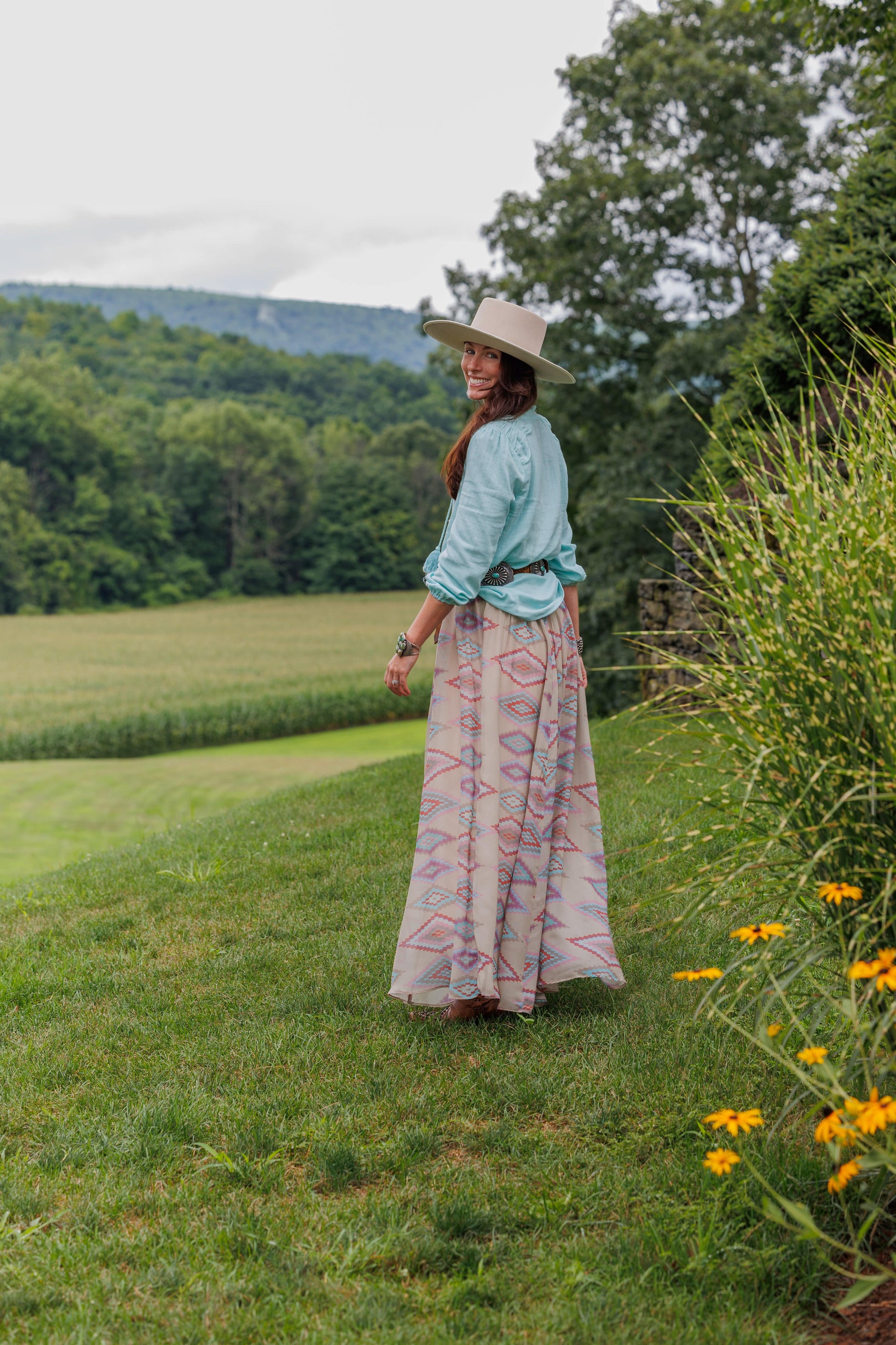 Woman in Toni Shirt and Sunny Skirt on a grassy hillside.
