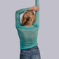 Woman in teal shirt and jeans, arms raised.