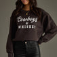 Woman wearing a brown Cowboys & Whiskey sweatshirt.