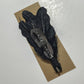 Black feather brooch on cardboard.