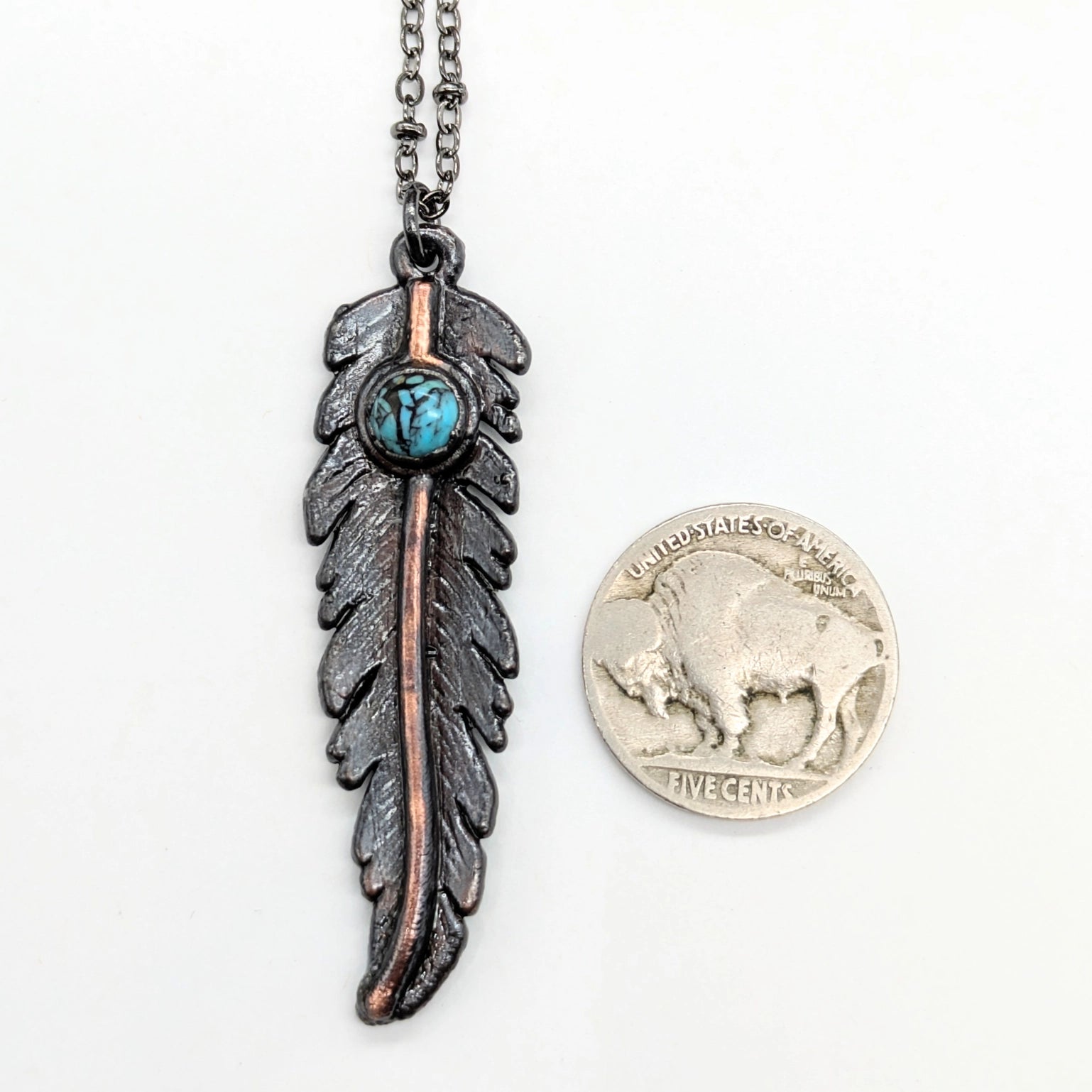 Feather pendant with turquoise accent next to buffalo nickel.