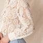 Woman wearing a white lace paisley shirt and blue pants.