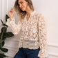 Woman wearing a cream lace blouse with long sleeves and blue jeans.