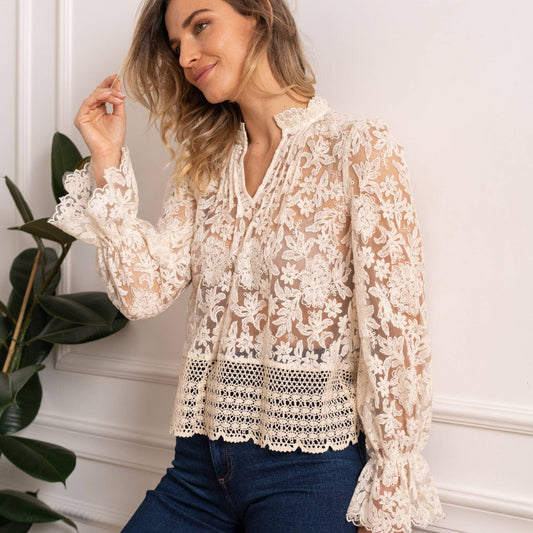 Woman wearing a cream lace blouse with long sleeves and blue jeans.