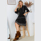 Woman wearing black dress and boots, seated on a stool.
