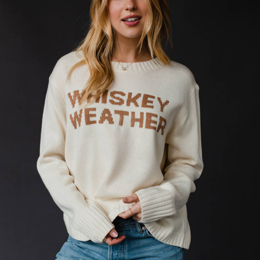 Woman wearing a cream sweater with Whiskey Weather text.