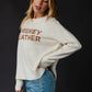 Woman wearing cream sweater with text.