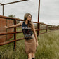 Cowgirl in fringe skirt leans on fence, 8L5A9519