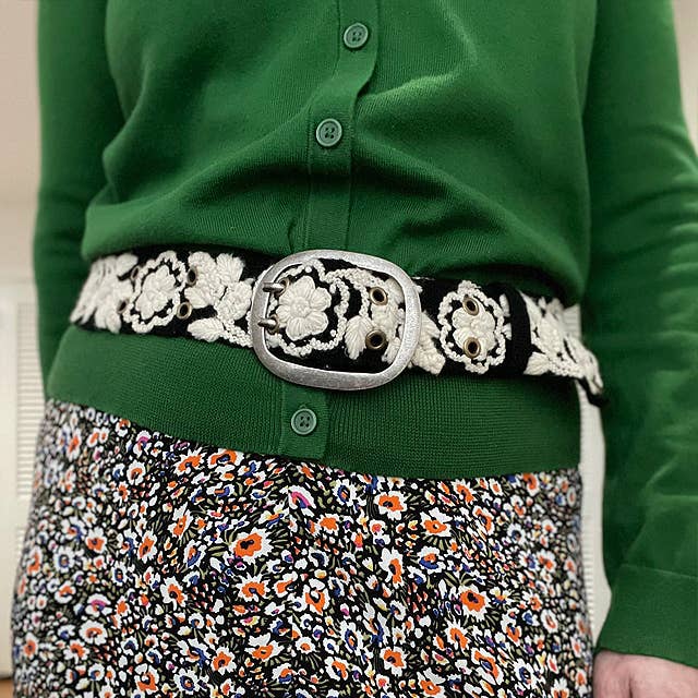 Green sweater, floral belt, and patterned skirt.