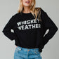 Woman wearing a black sweater with WHISKEY WEATHER on it.