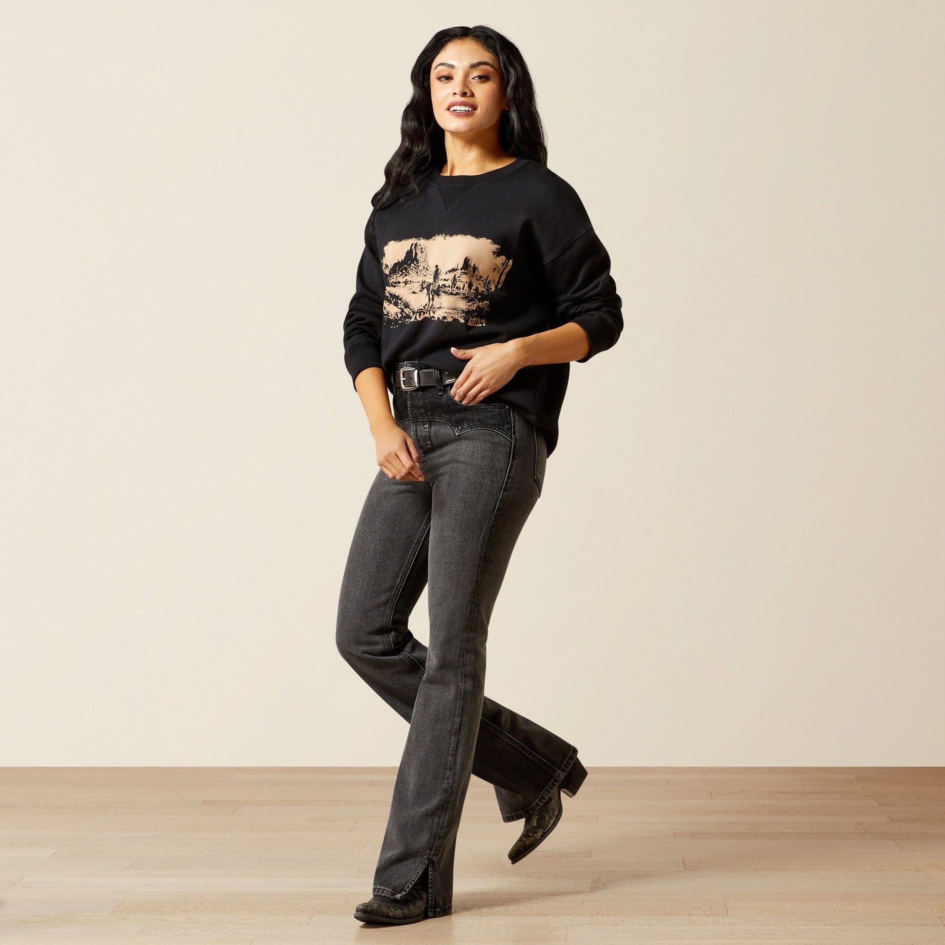 Woman in black sweatshirt and jeans, warm tones.