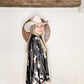 Woman in cowboy hat and patterned shirt smiling.