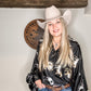 Woman in cowboy hat and shirt with horse print.