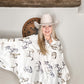 Woman in cowboy hat and horse-print shirt smiling.
