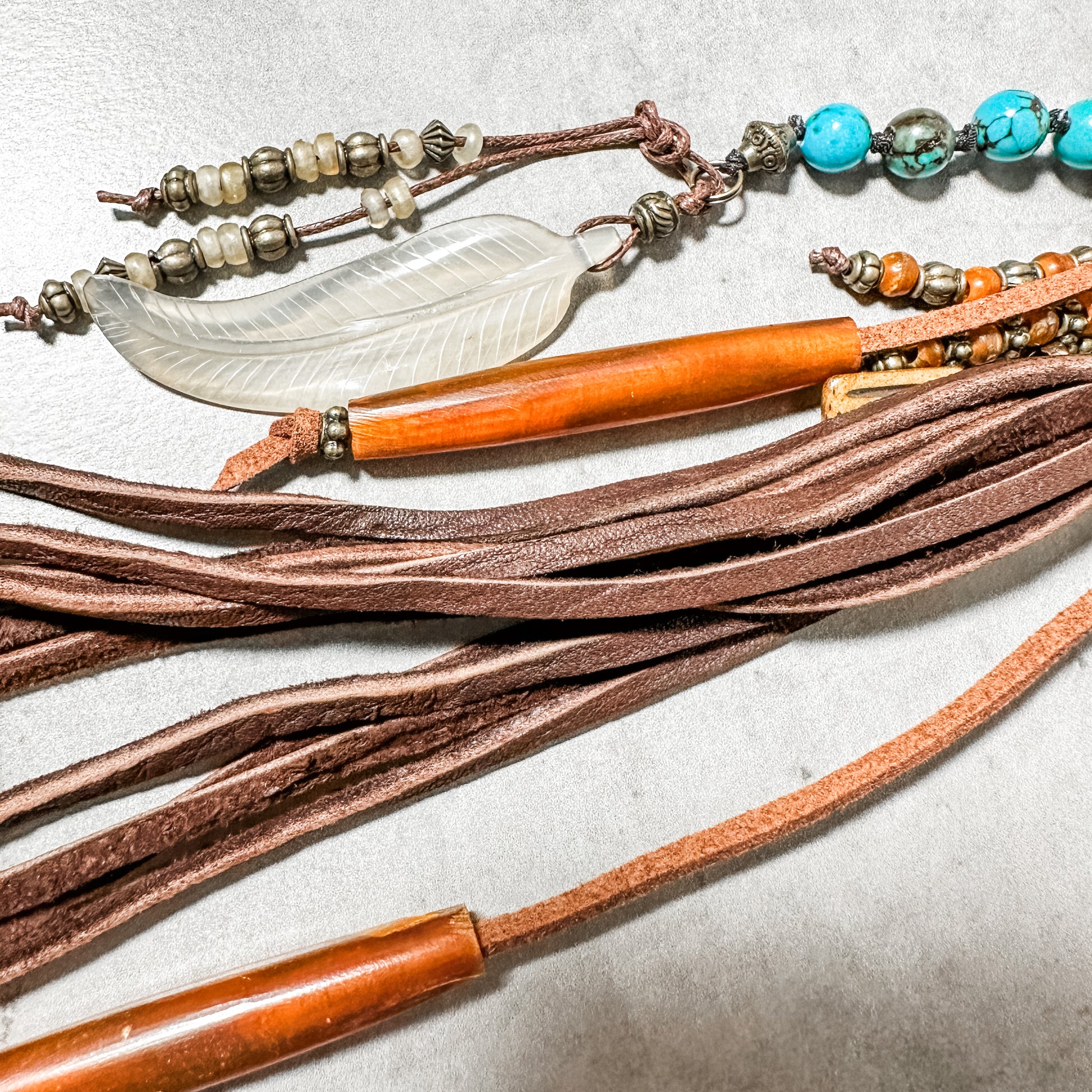 Close-up of a beaded necklace with leather strands and a feather pendant.