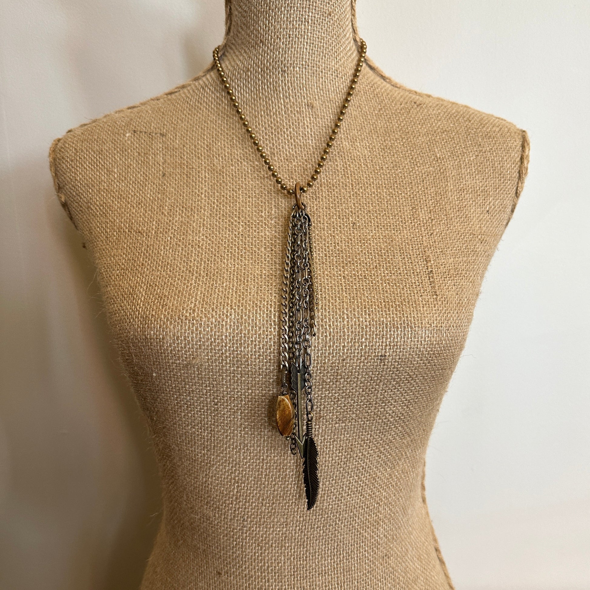 Necklace with chains, stone, and feather on a mannequin.