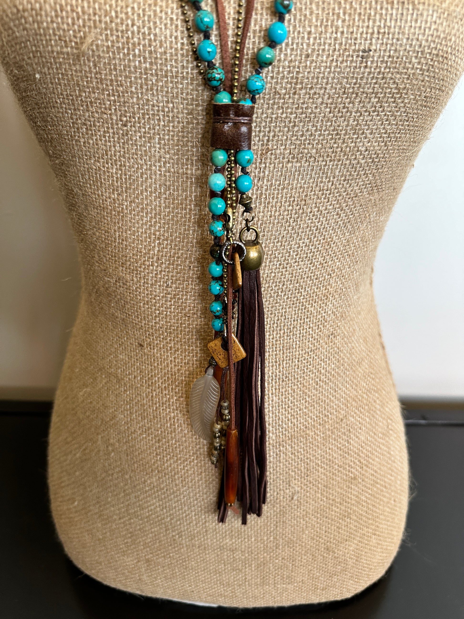 Turquoise beaded necklace with leather tassel on a mannequin.